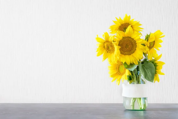 Bright yellow big sunflowers in glass vase on dark table on light texture background. Mockup banner with sunflower bouquet with copy space.