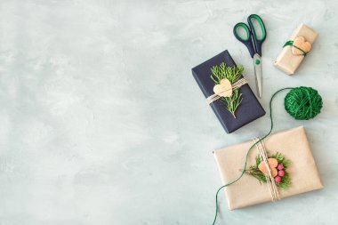 Noel kaydırma. Hediye kutusu, kağıt, sicim, iğne yapraklı dallar, kırmızı meyveler ve makas gri beton zemin üzerine sarma tekne ile mevcut. Noel hediye paketi kaydırma, süslemeleri, düz yatıyordu