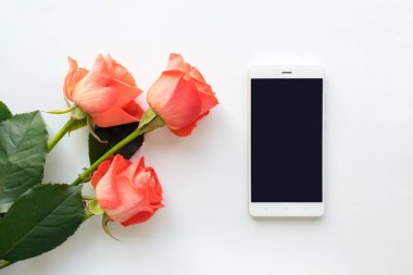 Beyaz arka plan üzerinde üstten görünüm kopya alanı ve gül ile cep telefonu. düz, alay yığmak. Kadının çalışma alanı ile telefon ve çiçekler.