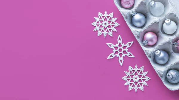 Modern minimalistic Christmas banner background. Pink and silver glitter Christmas tree ornaments in egg packages and shiny snowflakes on pink background mock up. Flat lay, top view