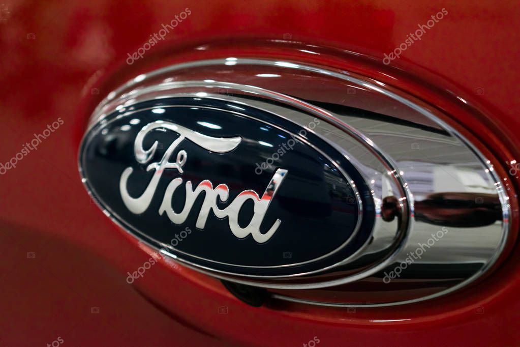 Close up Ford logo on new red car at motor show, Automobile Salon. Ford company logo, selective focus