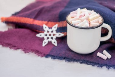 Kış konsepti. Marşmelovlu kahve ve mor yün atkıyla bembeyaz mineli metal bardakta dekoratif parlak kar tanesi. Soğuk havada ılık bir hafta sonu.