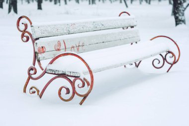 Şehir parkında kalp sembolü ile karla kaplı bank. Sahte metal ve ahşap park bankı ve ağaçlar yoğun kar ile kaplı. Kış tarihi, romantizm, Sevgililer Günü,