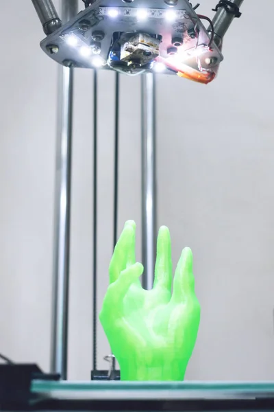 Green plastic 3D printed human hand stands in three-dimensional printer. Object model printed on automatic three dimensional 3d printer. Additive manufacturing and robotic automation technology.