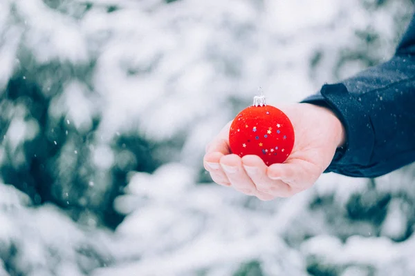 Close Man Hand Holding Red Christmas Ball Front Snow Covered — Stock Photo, Image