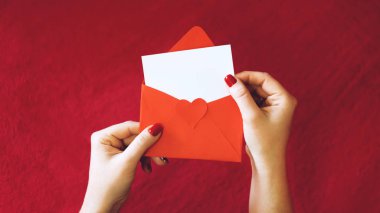 Sevgililer günü tebrik kartı, mockup kopya alanı ile. Kadın el boş beyaz kart ve kırmızı zemin üzerine kırmızı zarf. En az stili,