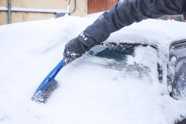 Man cleaning car from snow and ice with brush and scraper tool during snowfall. Winter emergency. Weather-related vehicle emergencies. Automobile covered with snow clipart