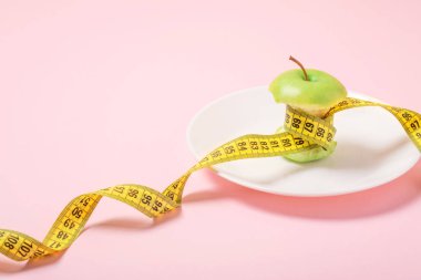 Bant yerine pembe bir arka plan üzerinde beyaz bir tabakta bel ölçüm ile Apple göbek. Diyet, kilo kaybı, açlık, fitness kavramı.