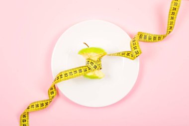 Bant yerine pembe bir arka plan üzerinde beyaz bir tabakta bel ölçüm ile Apple göbek. Diyet, kilo kaybı, açlık, fitness kavramı.