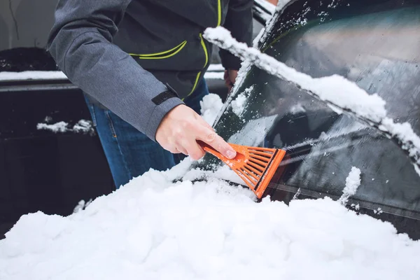 Man cleaning car from snow and ice with brush and scraper tool during snowfall. Winter emergency. Weather-related vehicle emergencies. Automobile covered with snow