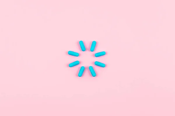 Bright blue pills in load symbol on pink background. Medicines,