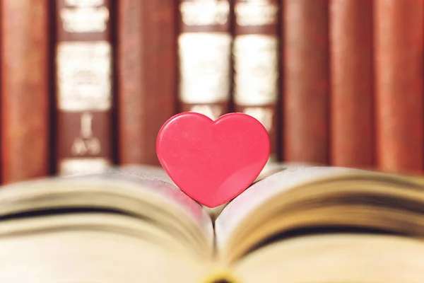 Open book with coral heart on the bookshelf background. Pink pla — Stock Photo, Image