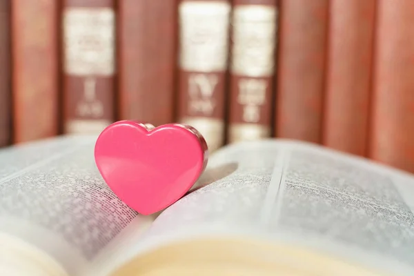 Open book with coral heart on the bookshelf background. Pink pla — Stock Photo, Image