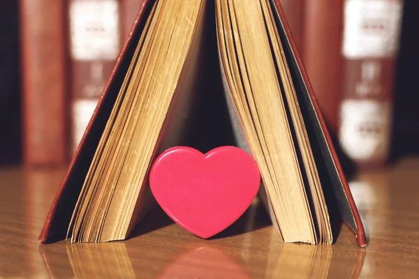 Open book with coral heart on the bookshelf background. Pink pla