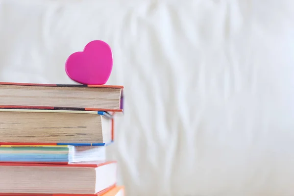 Stack of books and pink heart on the white bed. Education backgr — Stock Photo, Image