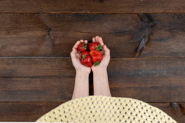 Strawberries in children hands. Baby girl in summer hat holding — Stock Photo, Image