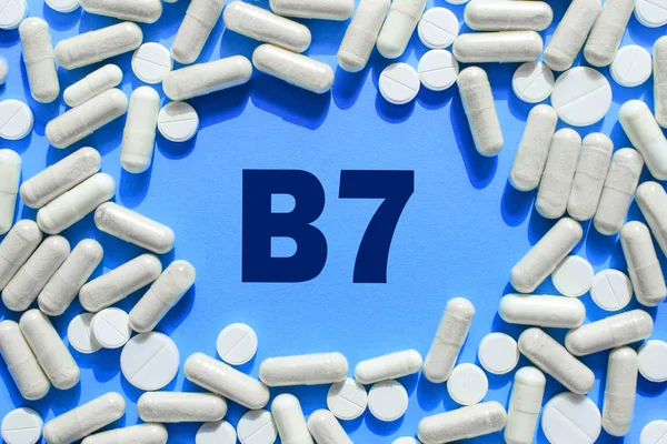 Texto de vitamina B7 em cápsulas brancas moldura em fundo azul. Comprimido — Fotografia de Stock