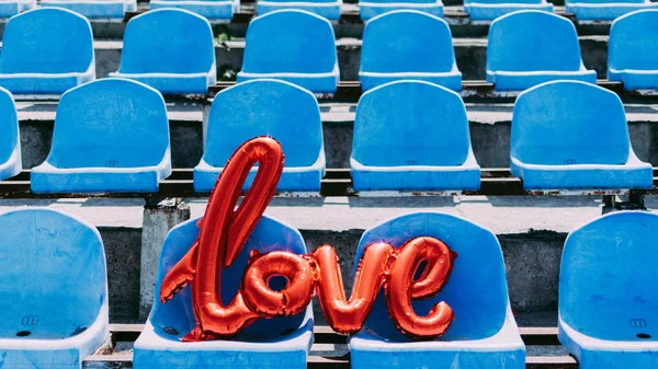Liebe rote Folienballons auf blauen Stadionsitzen. Ballo in Buchstabenform — Stockfoto