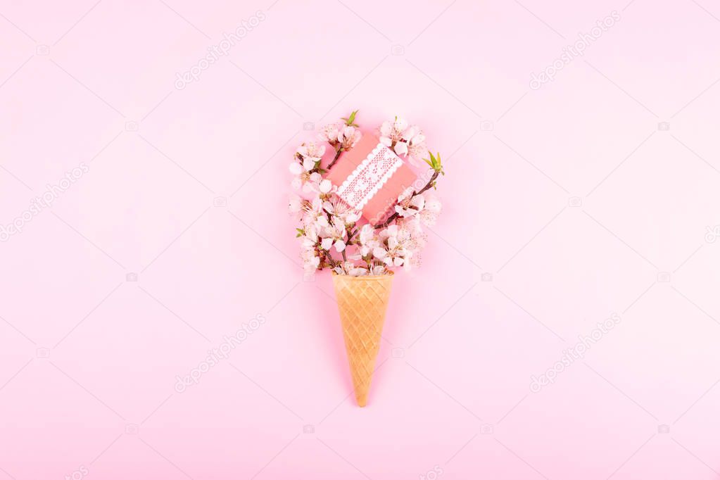 Ice cream waffle cone with colorful flowers and gift box on pink