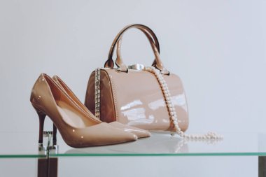 Bej yüksek topuklu ayakkabılar, dantelli el çantası ve rafta boncuklar. 