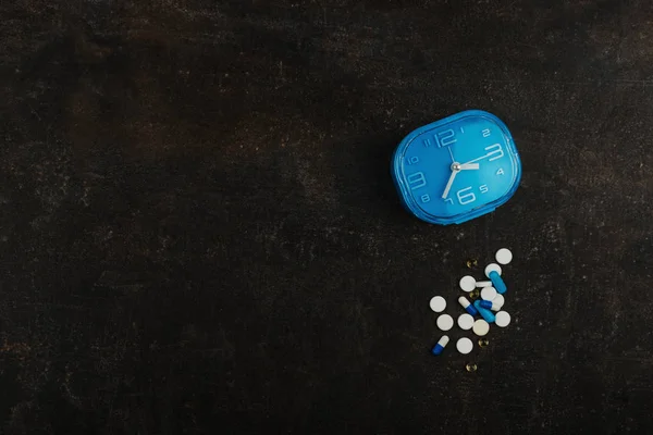 Comprimidos variados e relógio azul na mesa escura. medicamentos saudáveis — Fotografia de Stock