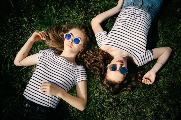两个戴着太阳镜的年轻女友躺在草地上 — 图库照片