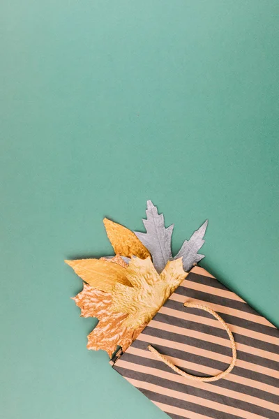 Autumn composition with golden leaves in gift bag on green paper