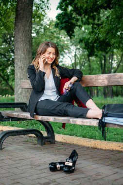 Aşırı çalışma, stres, özgürlük, iş bırakma kavramı. Çıplak ayaklı, yorgun bir kadın bankta oturuyor ve rahatlamayı seviyor..