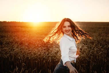 Haziran yaz gündönümü konsepti mutlu genç bir kadının silüeti buğday tarlasında sıcak altın saat gökyüzüne karşı dinleniyor..