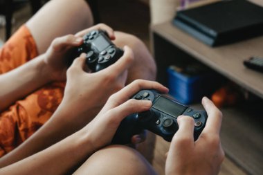 Playstation 'da online video oyunu oynayan iki çocuk. Ekranın önünde Joystick tutan iki genç..