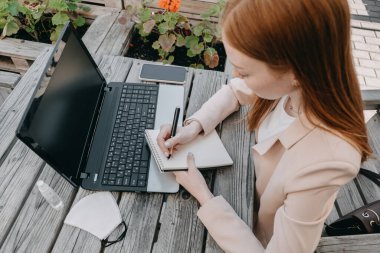 Dijital göçebe, serbest çalışan, yeni normal çalışma süreci. Caddedeki kafede dizüstü bilgisayarda çalışan genç kızıl saçlı kadın..