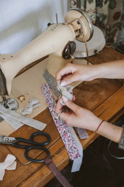 Küçük işletme fikirleri, yerel terzilik, eski moda terzilik çalışma alanı. Kadın moda tasarımcısı el işi kumaş saç aksesuarları, fiyonk, saç tokaları yapıyor. Dikiş makinesiyle çalışan terzi..