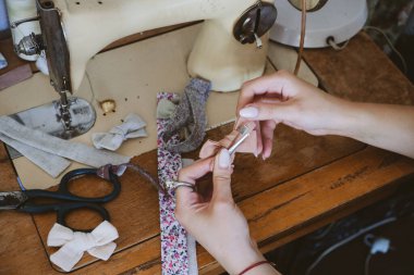 Küçük işletme fikirleri, yerel terzilik, eski moda terzilik çalışma alanı. Kadın moda tasarımcısı el işi kumaş saç aksesuarları, fiyonk, saç tokaları yapıyor. Dikiş makinesiyle çalışan terzi..