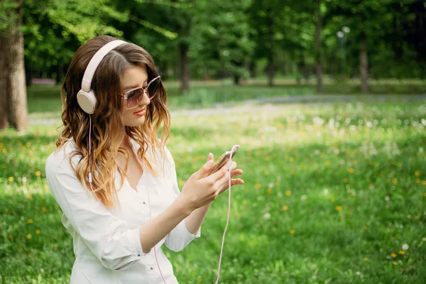 Language Learning, online study concept. Young girl in headphones and with a smartphone learns a foreign language in the park outdoor.