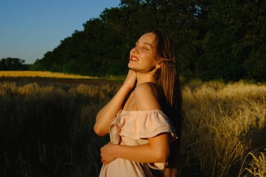 Dijital Detox, Ayrılma, Yaşam, Çevrimdışı, Doğaya duyarlılık, Farkındalık konsepti. Genç, sarışın, kaygısız, uzun saçlı, mavi keten elbiseli kız gün batımında buğday tarlasında hayatın tadını çıkarıyor.