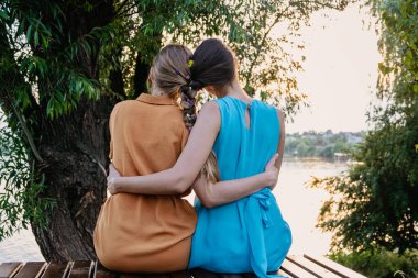 Kadın arkadaşlığı, çeşitlilik, destek, ortaklık, kız arkadaş konsepti. İki sarışın, esmer, örgülü örgülü örgü örgülü, gün batımı arka planında oturup sarılan iki kız..