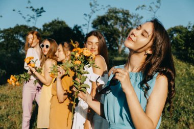 Kadın Eşitliği Günü, kız gücü, çeşitlilik, kadınlık kavramı. Doğada gül taşıyan beş mutlu genç bayandan oluşan bir grup. Açık hava kız arkadaşları parkta kutlama yapıyor.
