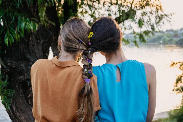 女性友谊的女性气质 多样化 伙伴关系 女朋友的概念 两个金发碧眼的女孩 一头乌黑的头发 戴着辫子 坐在自然日落的背景下拥抱在一起 — 图库照片