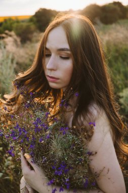 Ulusal Rahatlama Günü, gevşeme uygulamaları, akıl sağlığı, yavaş yaşam konsepti. Uzun rüzgarlı saçları ve çiçekli buketi olan genç kız günbatımının arka planında doğanın tadını çıkarıyor..