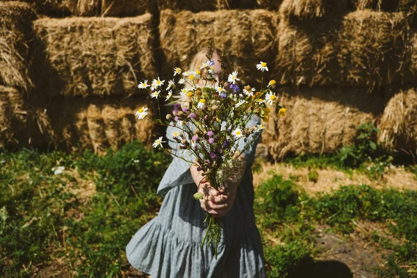 Young girl in rubber boots with flowers standing against the background of straw bales on country farm. Farming, Cottagecore, Farmcore, Countrycore aesthetics, fresh air, countryside, slow life — Stock Photo, Image