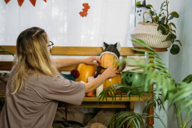 Genç bir kadın Cadılar Bayramı için evi dekore ediyor. Evin içi cadılar bayramı için dekore edilmiş DIY hayalet balonu ve doğal olarak ev bitkisi, sıfır atık tarzı