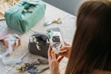 Elle paketlenmiş sıfır hediyenin fotoğrafını çeken bir kadın. Furoshiki Japon Hediye Paketi. Şükran Günü Sıfır İsrafı, çevre dostu hediye paketleme süreci, özel ders, adımlar.