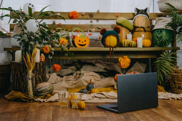 Halloween-Feste in neuen normalen, neuen Trick- oder Behandlungsvorschriften. Offener Laptop bereit für Online-Treffen, Jack O Lantern Halloween-Kürbisse, Kerzen, Girlanden und festliches Dekor auf einer Holzbank — Stockfoto