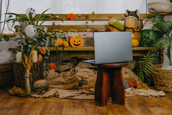 Halloween-Feste in neuen normalen, neuen Trick- oder Behandlungsvorschriften. Offener Laptop bereit für Online-Treffen, Jack O Lantern Halloween-Kürbisse, Kerzen, Girlanden und festliches Dekor auf einer Holzbank — Stockfoto