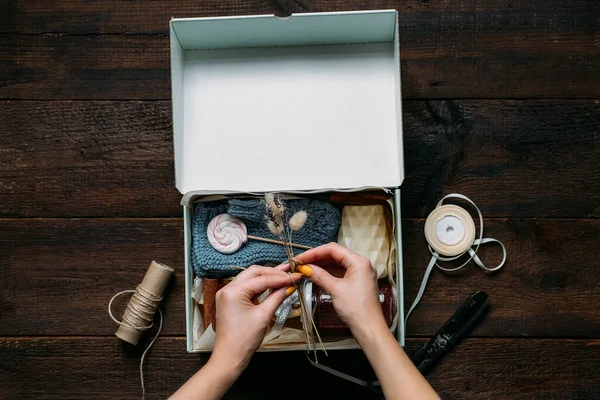 Caja de cuidado, ideas de paquetes. Las manos femeninas doblan una caja de cuidados con dulces y ropa de abrigo. Paquete de cuidado Entrega, Otoño Vacaciones de invierno Caja de regalo Food Care — Foto de Stock