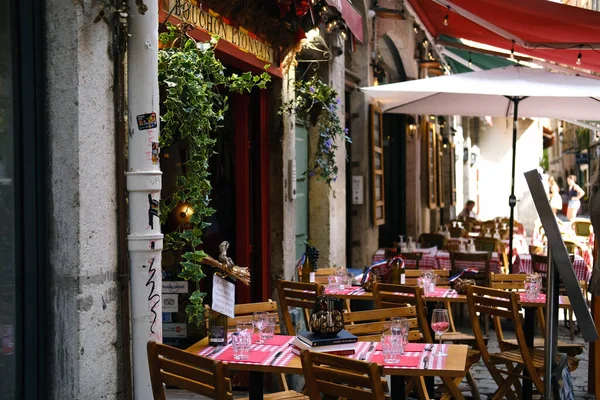 19 Ağustos 'ta Lyon, Fransa' da eski dar bir cadde boyunca kırmızı kareli masa örtüleri, ahşap sandalyeler, asılı bitkiler ve şemsiyelerle geleneksel bir Bouchon Lyonnais restoranının açık hava koltukları.