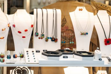 El yapımı cam mücevherler, küpeler, kolyeler, yüzükler ve butik vitrinlere dizilmiş kolyeler. Kasıtlı tasarım, anlamlı lüks, zanaatkarlık, anti-kitle üretimi