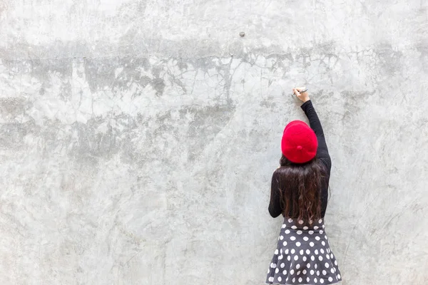 stock image Beautiful woman is drawing or writing some text, picture or commercial by using a pen. Gorgeous woman writes on beautiful cement wall. Pretty girl wears skirt, red hat, long sleeves shirt. copy space