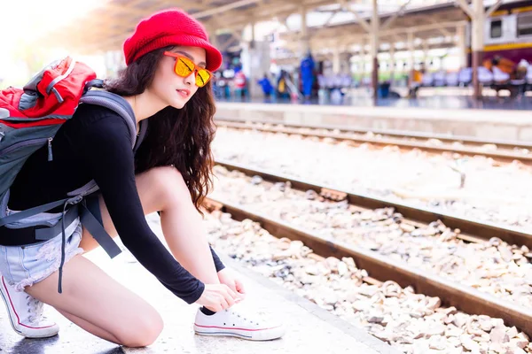 Attractive beautiful woman ties her shoelace while beautiful backpacker woman is waiting train for going to tourism location or destination. Gorgeous woman wears sunglasses and backpack. copy space