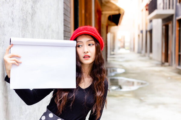 Charming beautiful woman is looking at empty paper or copy space. Gorgeous woman holds book of drawing at the town. Attractive beautiful woman acts like a amazing, admiring, like or love advertising
